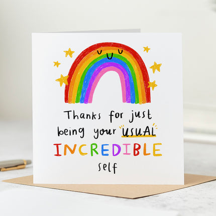 A folded white card that says 'Thanks for just being your usual incredible self' with a rainbow surrounded by stars