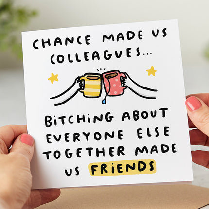White greeting card that reads 'Chance Made Us Colleagues... Bitching About Everyone Else Made Us Friends' with a playful illustration of two hands holding mugs of tea in a 'cheers' action.