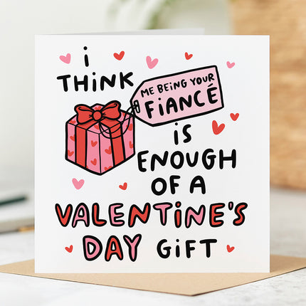 White greeting card that reads 'I Think Me Being Your Fiancé Is Enough Of A Valentine's Day Gift' with pink and red hearts.