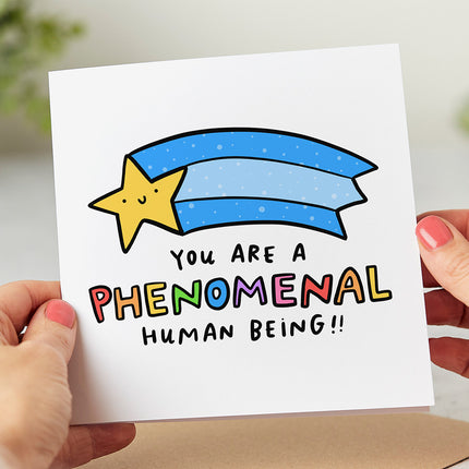White greeting card with a playful illustration of a shooting star followed by the text 'You Are A Phenomenal Human Being!!'