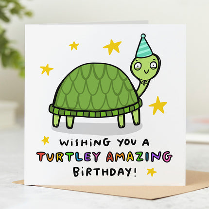 Greeting card with a fun illustration of a turtle wearing a party hat, surrounded by stars. The text below is written in a playful font and reads 'Wishing You A Turtley Amazing Birthday'.
