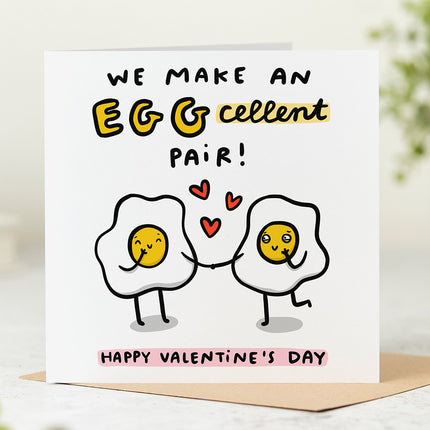 Greeting card with a playful illustration of two eggs holding hands. The text above reads 'We Make An Eggcellent Pair' and the text below reads 'Happy Valentine's Day'.
