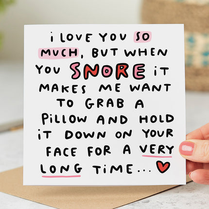 Funny greeting card that reads 'I Love You So Much, But When You Snore It Makes Me Want To Grab A Pillow And Hold It Down On Your Face For A Very Long Time...' with a  red heart.