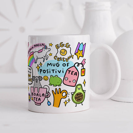 Image of a white ceramic mug with the words 'Mug of Positivi-Tea' written in playful lettering. The mug is decorated with various colourful illustrations and positive puns.