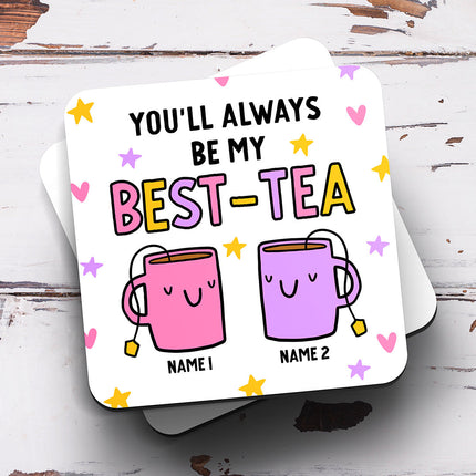 A square coaster with the text "You'll Always Be My Best-Tea" written in a black, pink, yellow and purple font. Below the text, there is an image of two mugs with stars and hearts around them. The coaster can be personalised with two names beneath each mug image.