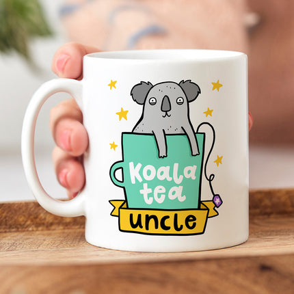 Front view of a white ceramic mug with an illustration of a koala in a teacup surrounded by stars. The text reads 'Koala Tea Uncle'.