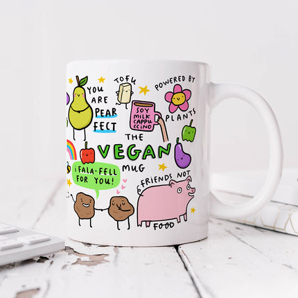 A white ceramic mug with colourful illustrations of various plant-based foods and witty vegan puns.
