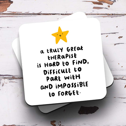 A white coaster with a yellow smiley star image and the text "A Truly Great Therapist Is Hard To Find, Difficult To Part With And Impossible To Forget" in a black quirky font.